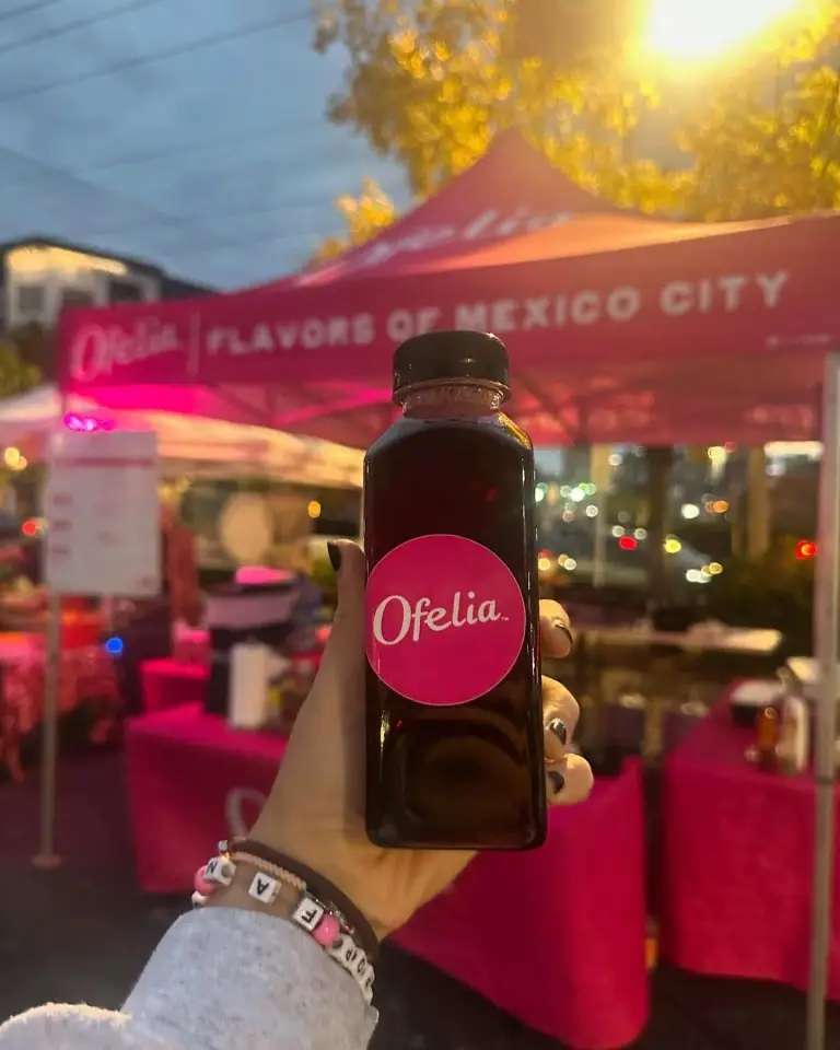 A hand holds a bottle of "Ofelia" juice at a vendor tent at the East Nashville Farmers Market