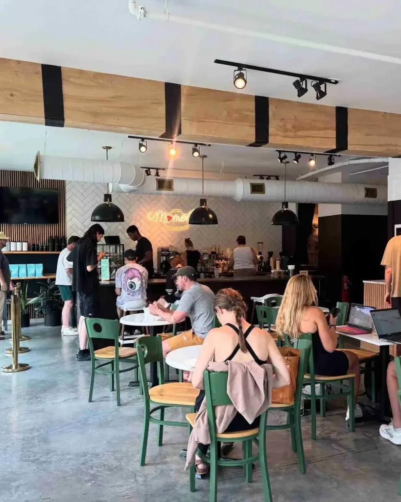 Patrons relax at tables near the counter and neon sign inside All People Coffee Nashville