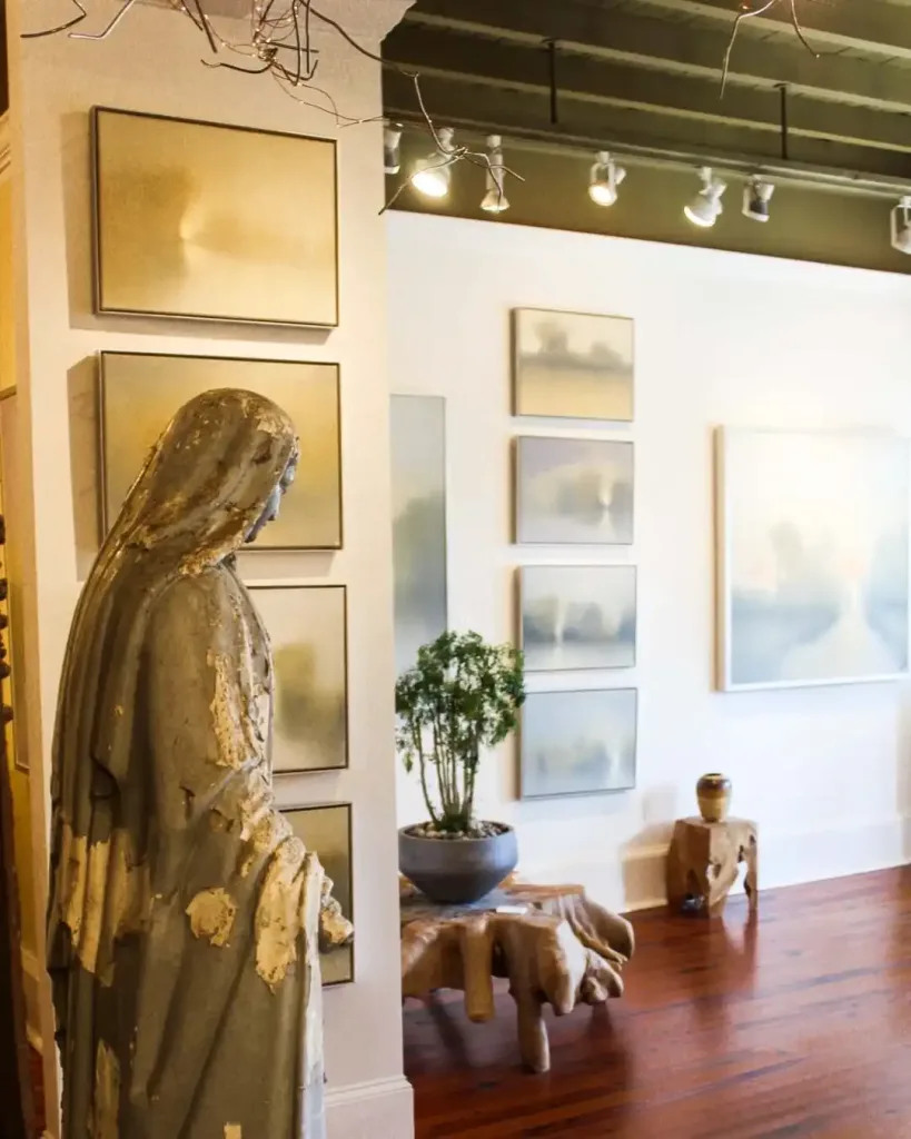 A solemn statue overlooks paintings inside a gallery during the First Saturday Art Crawl, a Free Summer Activities To Do in Nashville