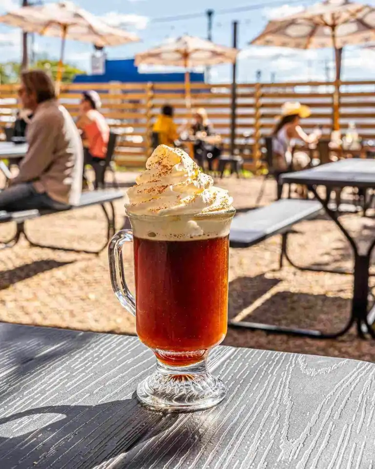 A tall glass mug of hot coffee topped with whipped cream on the sunny patio at Hearts Nashville.

