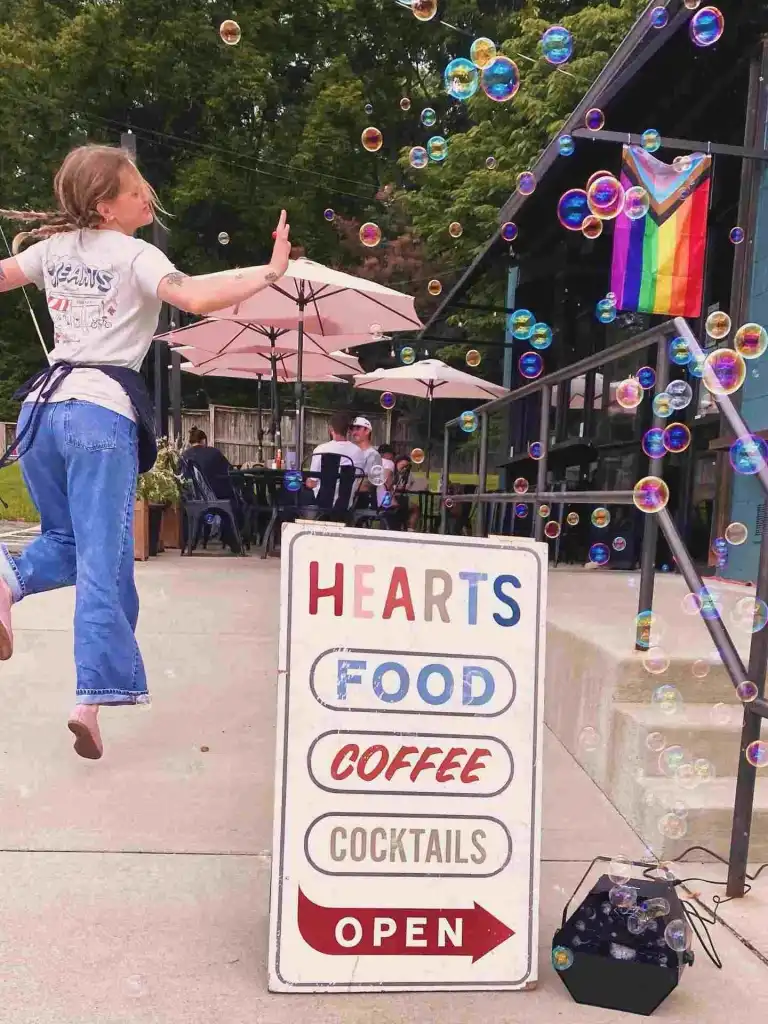 A person jumps playfully amidst bubbles next to a sign for Hearts Nashville, showcasing food, coffee, and cocktails.
