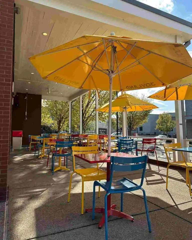 Colorful blue, yellow, and red chairs and tables under bright umbrellas at Joyland Nashville
