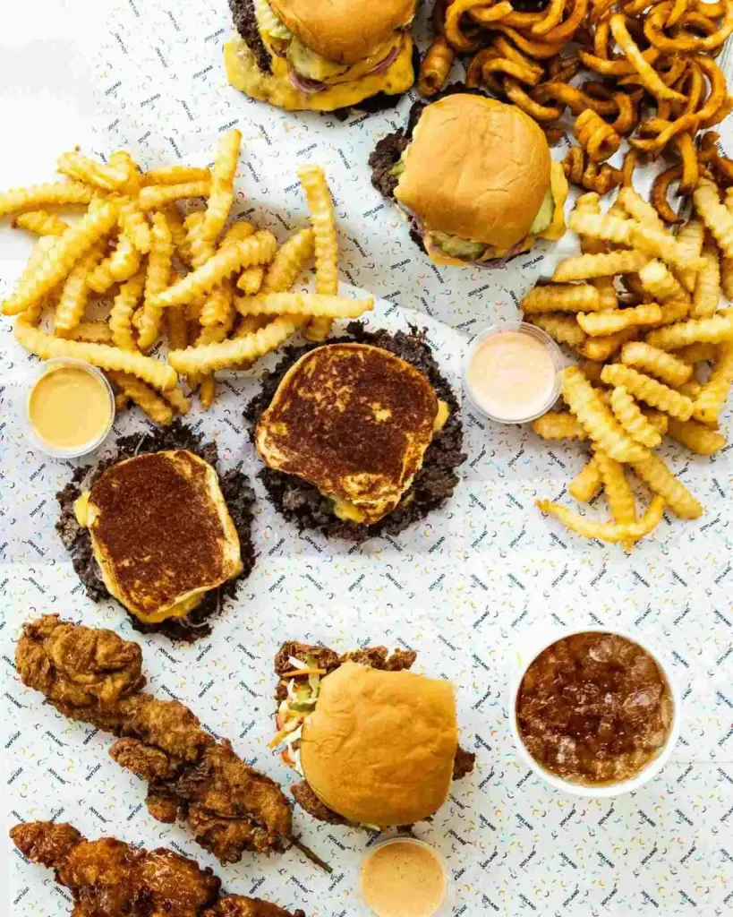 Grilled cheese, burgers, and curly fries are spread across a table at Joyland Nashville