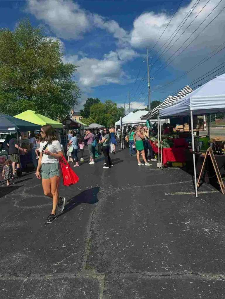 A crowd walks among vendor tents on a sunny afternoon at the East Nashville Farmers Market