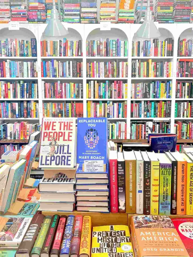A display of diverse new books sits before white arched bookshelves at The Bookshop Nashville