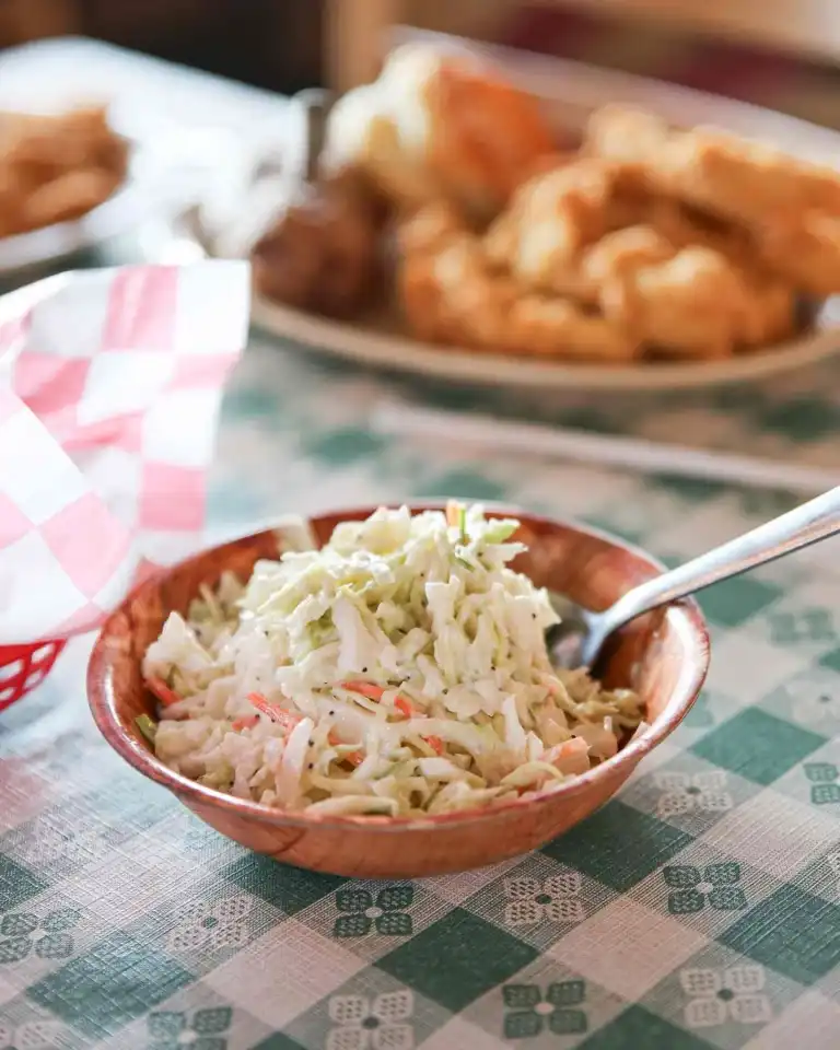 A wooden bowl of creamy coleslaw on a green checkered tablecloth, a side dish at Spicy Boys Nashville