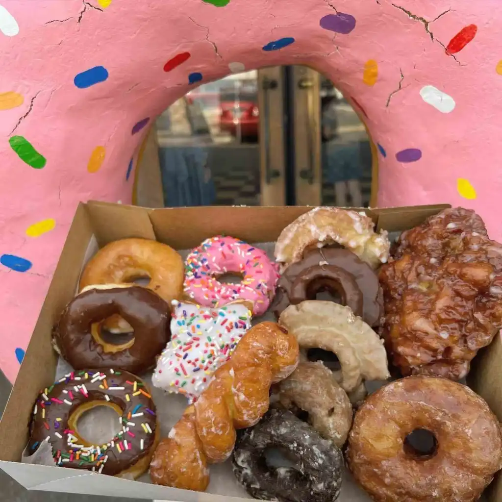 A box of assorted glazed and sprinkled donuts peeks through the giant pink donut hole at Fox's Donut Den Nashville