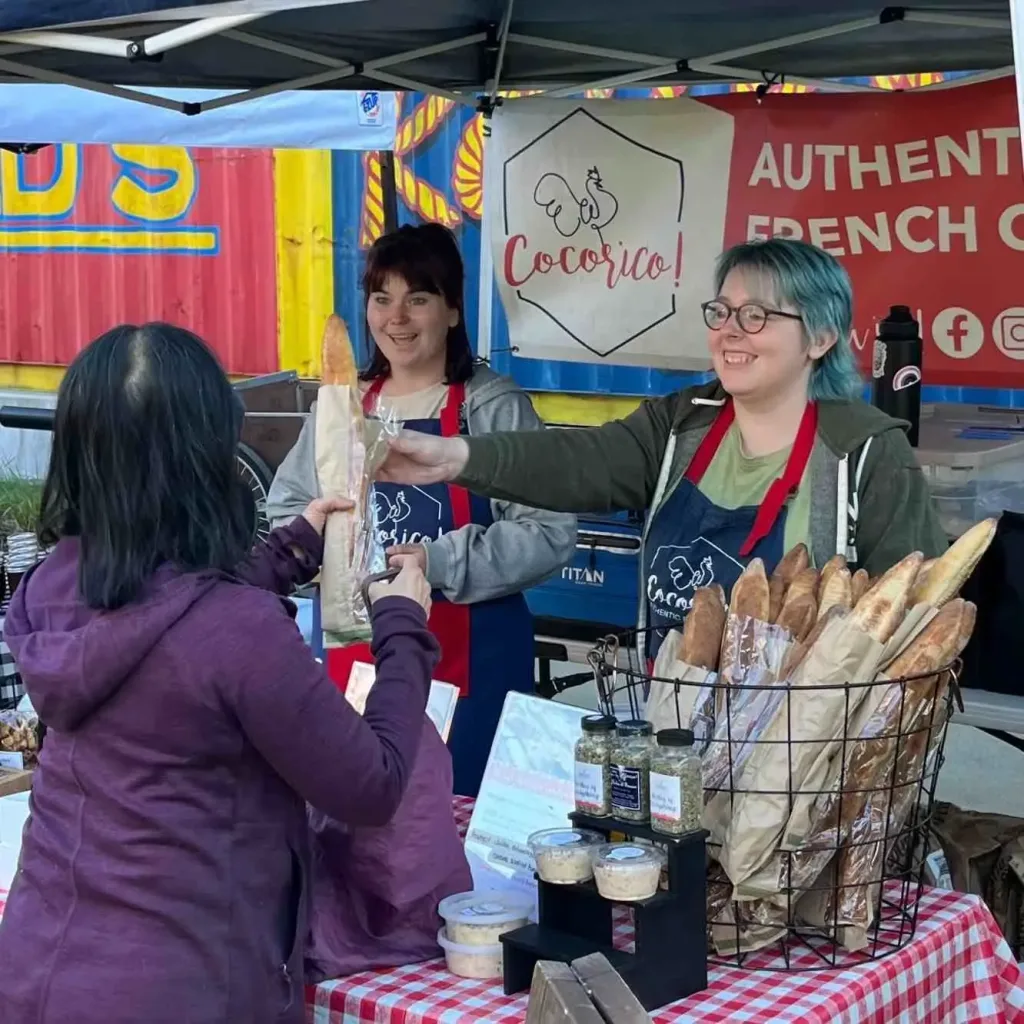 A vendor sells fresh French bread to a customer at the East Nashville Farmers Market