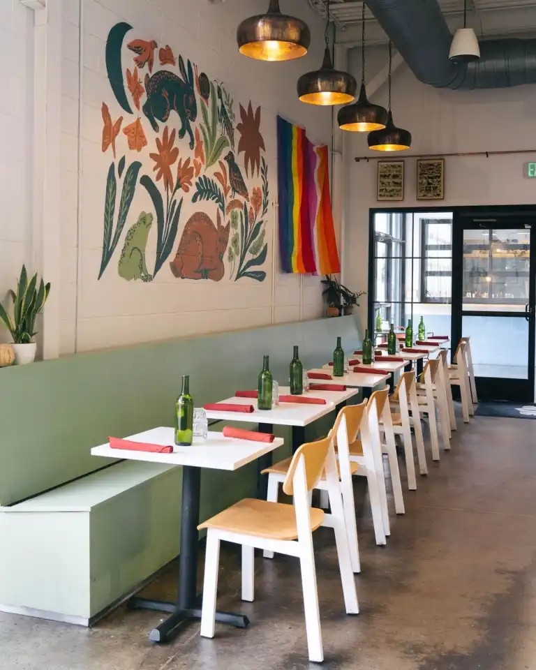 Dining tables line a green banquette beneath a vibrant nature mural at Flora and Fauna Nashville