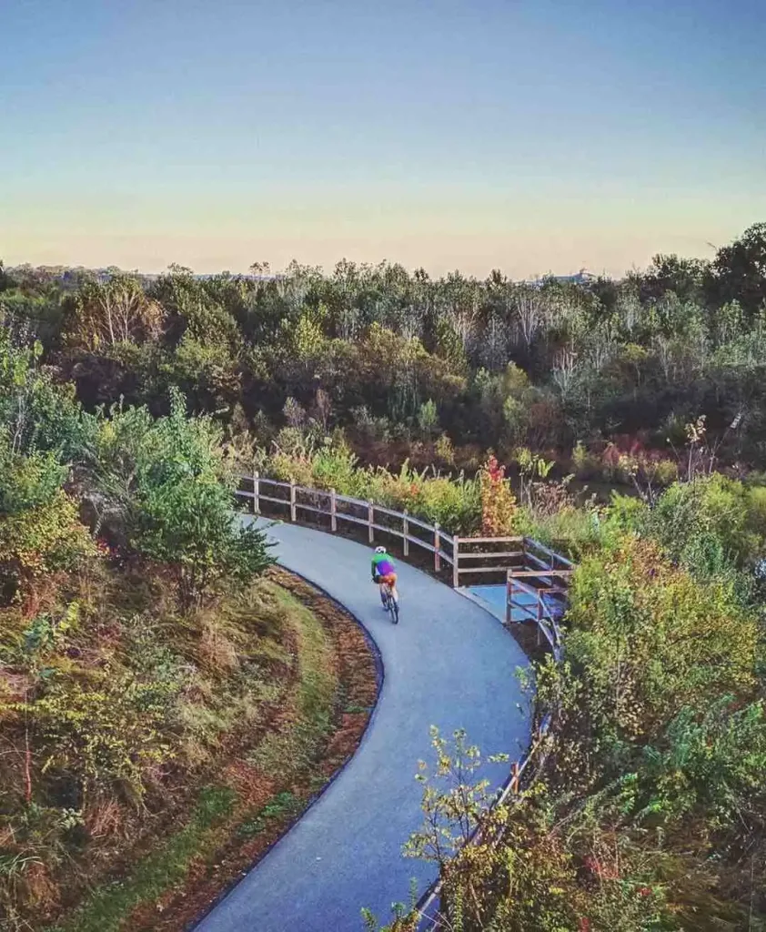 East Nashville Summer Bucket List Guide A cyclist rides on a paved path through lush green woods, a scenic activity for the East Nashville Summer Bucket List.