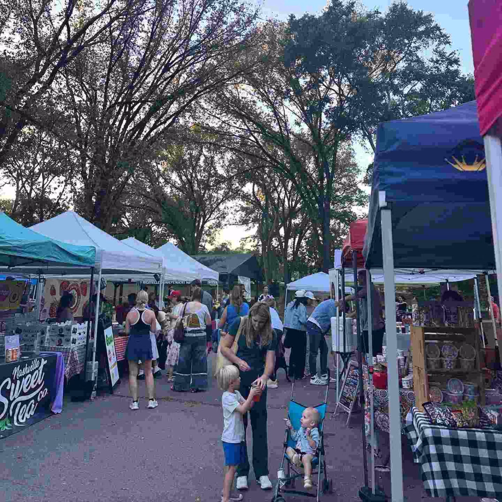 A crowd of people browses tents at a vibrant outdoor market, a classic experience in the Nashville 12 South area.