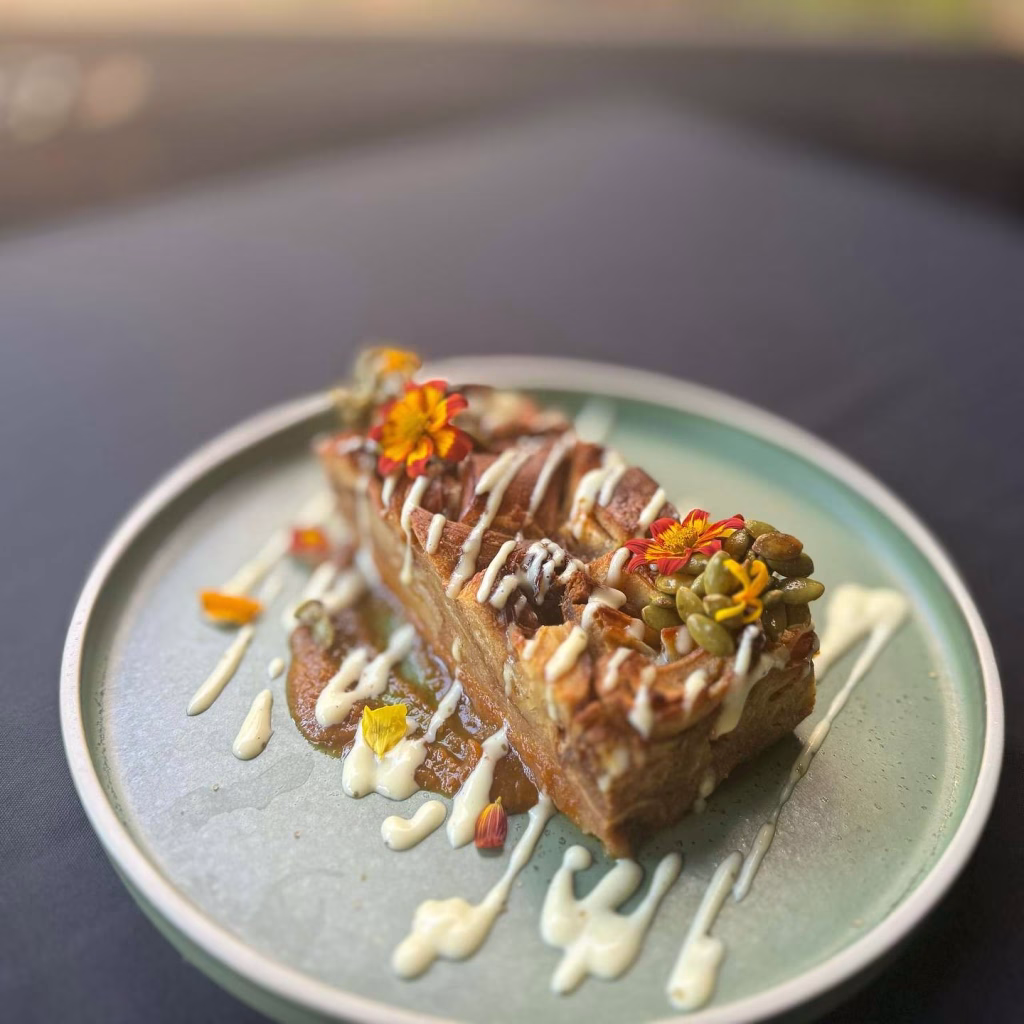 
A beautifully plated dessert of bread pudding drizzled with white sauce and topped with edible flowers at Urban Grub in Nashville 12 South.